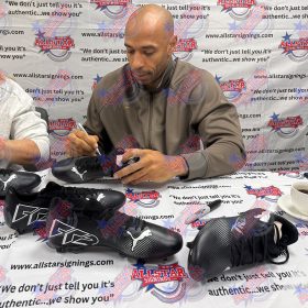Man signing black Puma soccer cleats at a signing event with an AllStar Signings backdrop.