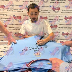 Man signs a light blue sports jersey at a fan signing event, backdrop says All Star Signings and authentic.”