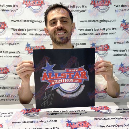 Man smiling while holding a black poster featuring the Allstar Signings logo, in front of an Allstar Signings backdrop.