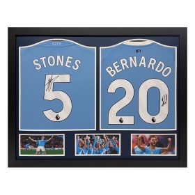 Framed display of Manchester City jerseys for Stones number 5 and Bernardo Silva number 20 with signatures and three small photos below.
