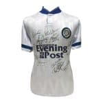 Λευκή φανέλα της Leeds United με μπλε φινίρισμα, καλυμμένη με υπογραφές και το λογότυπο του χορηγού της Evening Post.